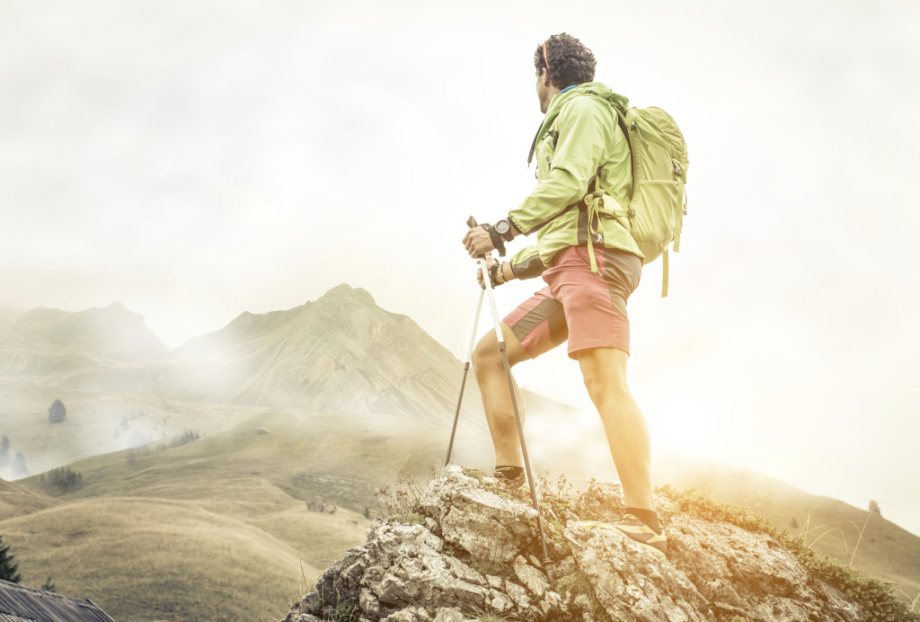 hiker climbing on the mountains. he stays on the top of a rock and watch his goal.
